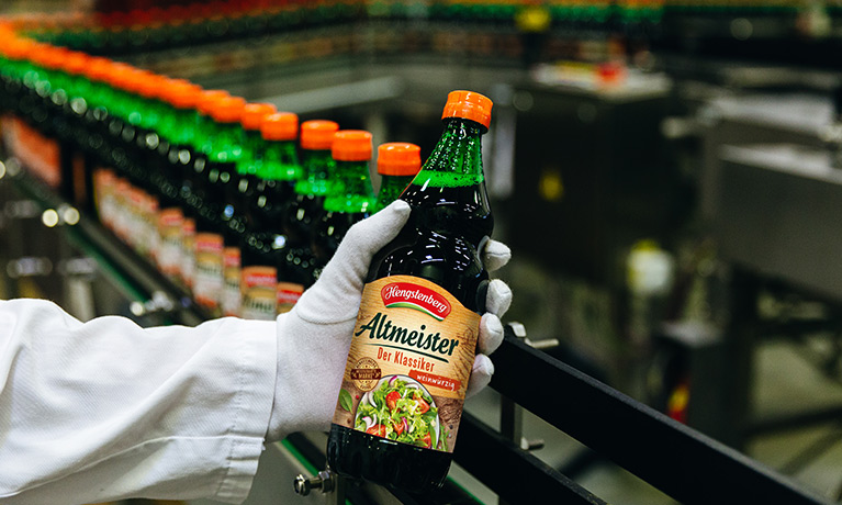 Una mano sostiene una botella de vinagre Altmeister.